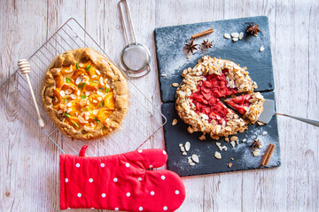 Apricot and strawberry galette placed on wooden table with cooking tools on the side.