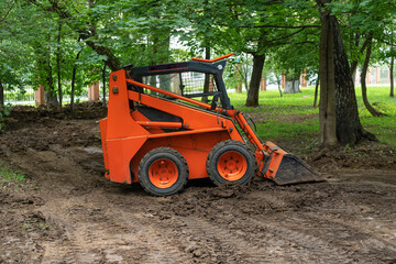 Mini bulldozer or skid steer loader working with earth in public park and performing landscaping works. © Viktoria