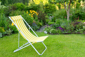 Beautiful flower garden with green lawn and yellow garden chair on it in summer