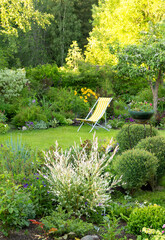 Beautiful flower garden with green lawn and yellow garden chair on it in summer, vertical...