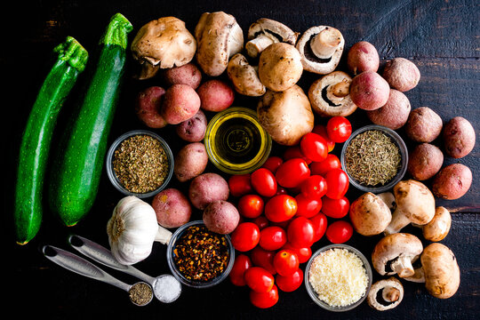 Italian Oven Roasted Vegetables Ingredients On A Wood Table: Grape Tomatoes, Zucchini, Mushrooms, Red Potatoes, Herbs, Spices, And Olive Oil