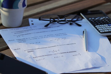 Ejercicios de matemáticas encima de una mesa de madera con calculadora , bolígrafo y gafas encima.