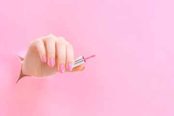 brush with nail polish in the hand of a young woman on a pink background from the hole.