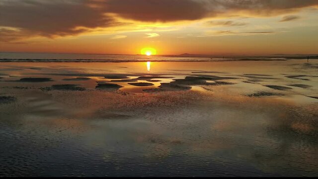 Bella puesta de sol en el mar con reflejos del cielo anaranjado vista desde la playa h&uacute;meda
