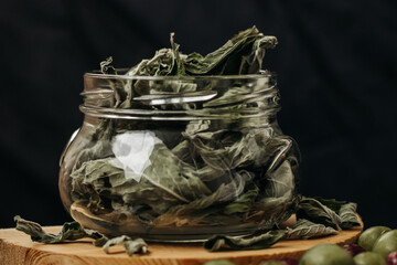 Glass jar with dry mint leaves on a black background. Tea leaves in a glass jar. Glass jar on a wooden table. Black background