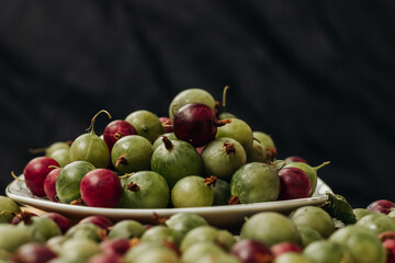 Green and red gooseberry berries on a black background. Gooseberries on a white plate on a black background