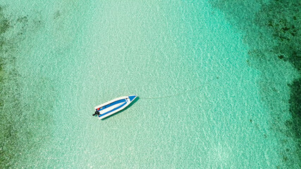 Turquoise lagoon witn boat. Surface on atoll and coral reef, copy space for text. Top view transparent turquoise ocean water surface.