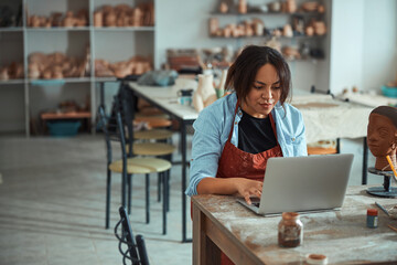 Charming female potter using notebook in pottery workshop