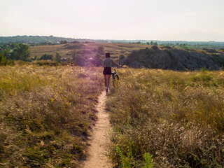 Obraz premium girl in green t-shirt with a bike in the field, against the backdrop of rocks, city