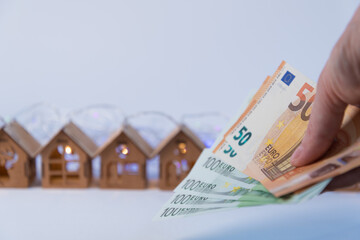 Lovely wooden houses, Christmas garlands, stand in a row. In the foreground is the hand holding the euro. Home purchase concept. Investments in real estate