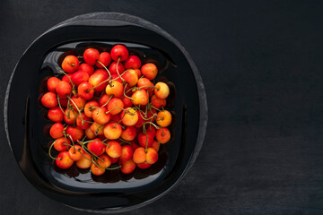 Ripe cherries in plate on black background top view. Sweet juicy cherries. Top view, copy space