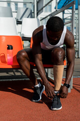 A male African American track and field athlete sits on a bench puts on a sports stocking before the race