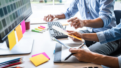 Two colleague creative graphic designer working on color selection and color swatches, drawing on graphics tablet at workplace with work tools and accessories