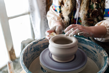 a potter in traditional antique clothes creates a pot of clay
