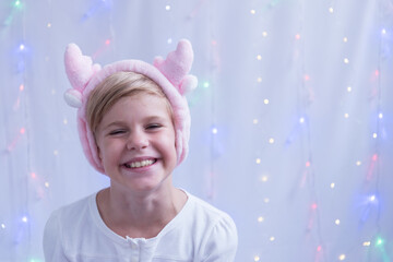 The child with blond hair smiles cheerfully. A girl in a hat shaped like a deer horn. Portrait of a happy child. Preparing for the new year and christmas. Merry christmas concept. Waiting for gifts