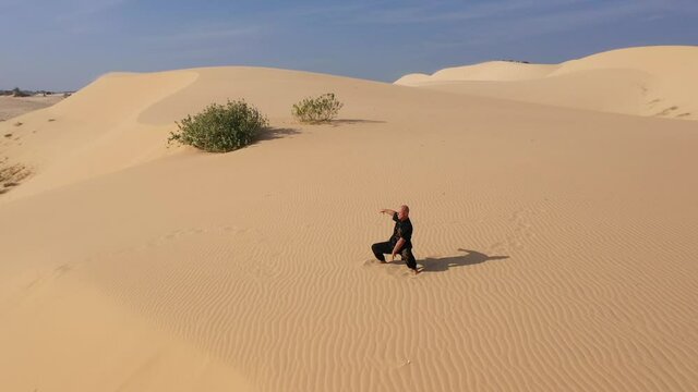 Old man in black is engaged in kung fu in the dunes at sunset. a lot of sand, golden sunset light. sports training. handsome man meditating. sensei training in desert. aerial view