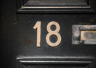 Number 18 eighteen in brass numerals on gloss black front door with letterbox visible. Shiny and...