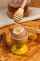 top, front view, very close distance of a soft boiled egg with top cut off  with Chile infused honey dripping from a wood applicator, in yellow, ceramic , egg holder, with toast on rare wood plater