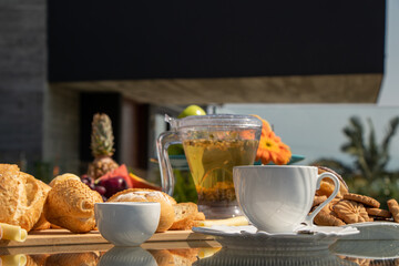 afternoon tea served in a transparent kettle, with bread, jam, cheese and ham and donuts with light sky and palm trees in the background
