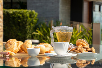 afternoon tea served in a transparent kettle, with bread, jam, cheese and ham and donuts with clear skies and green plants in the background