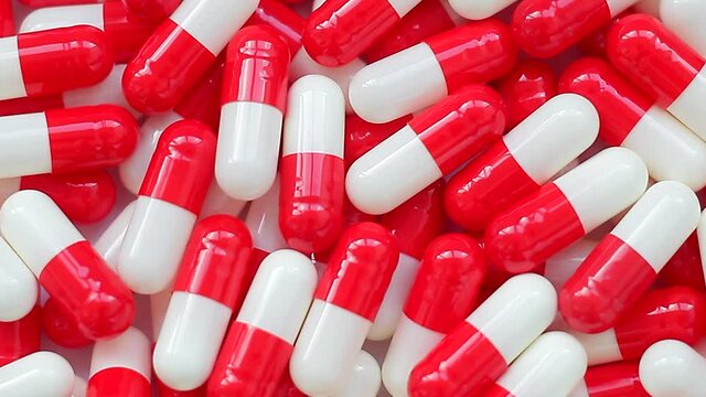 Seamless loop, backdrop, background texture, intro. Slow rotation of white and red  capsules, tablet flat lay, close-up.