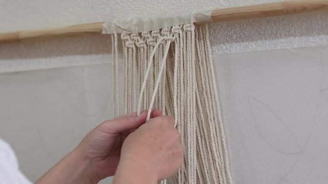 The base knots of macrame, the view from behind the shoulder close-up of the women hands, she ties knots. ECO friendly modern knitting DIY natural decoration concept.