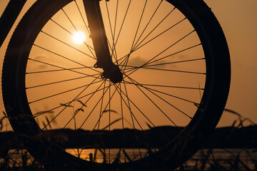 Close-up silhouette of a bike wheel at sunset. The sun shines through the wheel of a bicycle, selective focus