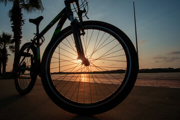 Fototapeta na wymiar Silhouette of a bike at sunset. The sun shines through the bicycle wheel at the sea side park