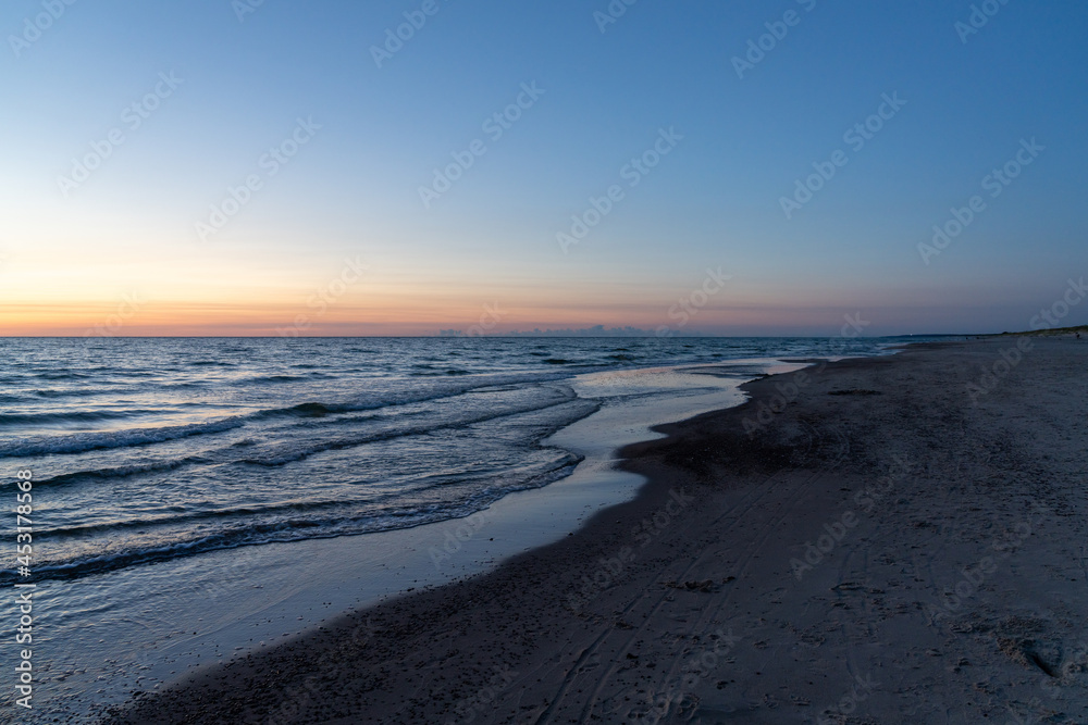 Sticker ocean sunset with sandy beach and wooden pylon storm groin in the foreground