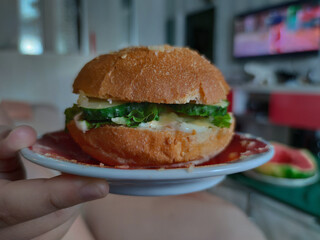 Burger with cheese, cutlet and herbs on a plate. Homemade burger, cooking. Food intake. Food on the table. Delicious junk.