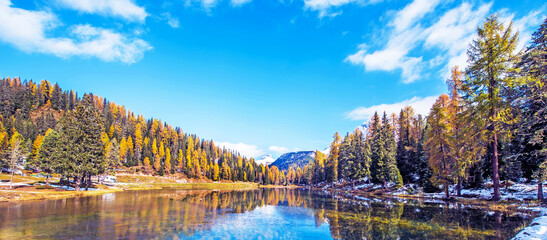 Fantastic autumn landscape with a light crust on the surface of the pondbig stone and yellow larch on a background of snowy mountains in the Antorno Lake, Dolomites. Exotic amazing places.