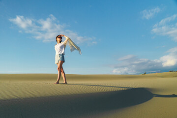 Woman standing on wavy sand dunes in desert landscape at sunset light and wind.
