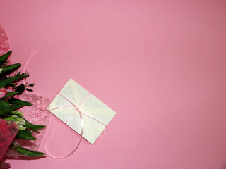 a bouquet of tulips and a gift envelope on a pink background copy space