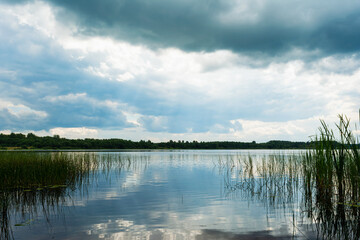 View from the coastline to the blue lake. Summer cloudy day. Nature landscape background