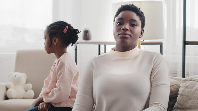 Afro american offended mother black woman ethnic mommy sitting at home turned away from little daughter girl child feels sad after quarrel conflict resentment generation problem misunderstanding abuse