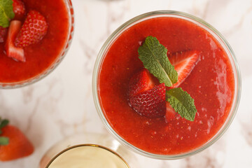 Several glasses with traditional creamy pudding dessert panna cotta with peppermint and strawberry jam surrounded fresh strawberries on a marble surface, top view