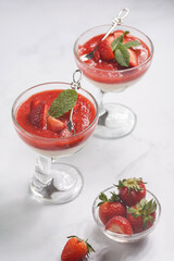 Several glasses with traditional creamy pudding dessert panna cotta with peppermint and strawberry jam surrounded fresh strawberries on a white surface