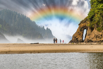 Family adults and children walking on the ocean beach with incredible sunlit rainbow sky and sun rays in the early morning mist.