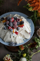 Pavlova meringue with whipped cream and frozen berries, raspberries, blackberries, blueberries and strawberries. Airy cake on a wooden stand among the floral decoration.