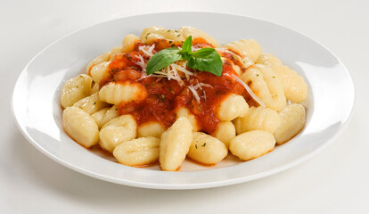 Nhoque ao molho de tomate com queijo parmesão e folha de manjericão, no fundo branco para recorte.