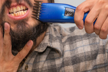 A man shaves his beard with an electric machine baring his teeth