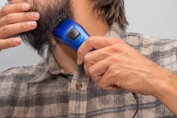 The man put a shaving machine to the neck near the beard