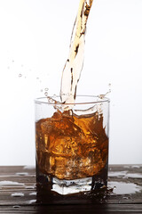 A glass of amber colored liquor like liquid falling into a glass with ice cubes.