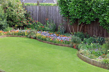Brightly Coloured Summer Flowers In A Garden Border Surrounded By A Wooden Fence With A Well Maintained Lawn.