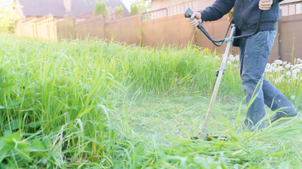 man mows grass with trimmer, focus on foreground blurred background