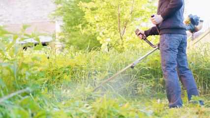 man mows grass with trimmer, focus on foreground blurred background