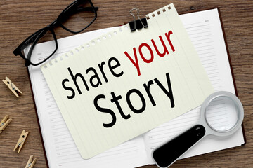 Share Your Story, notepad with text on a wooden table. notebook near black glasses