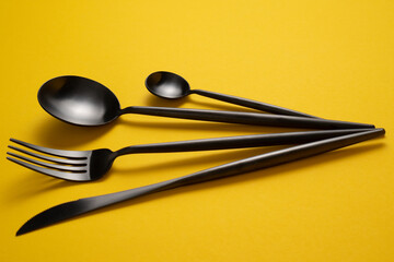 Black tableware on yellow tablecloth. Black flatware on yellow tablecloth. Black cutlery on yellow tablecloth