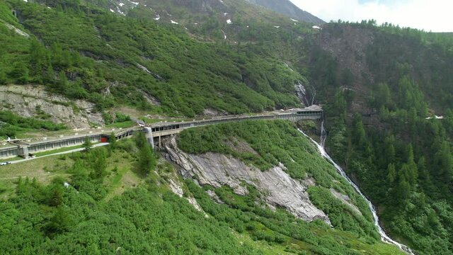 AERIAL Cinematic drone point of view of the Simplon pass in the picturesque mountains of Switzerland. Flying along a covered mountain pass in the vibrant green Swiss Alps. Scenic route across mountain