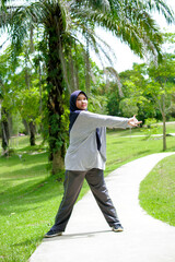 A portrait of a Muslim woman wearing sporting clothes is doing a healthy activity in a park.
